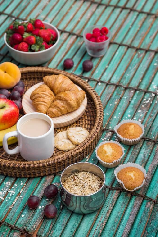 Caf&eacute; da manh&atilde; &eacute; umas das minhas refei&ccedil;&otilde;es preferidas, mas sei que para muita gente &eacute; um desafio montar um caf&eacute; da manh&atilde; nutritivo e gostoso, ent&atilde;o no texto de hoje vamos falar tudo sobre caf&eacute; da manh&atilde;, e para come&ccedil;ar:

Por que o caf&eacute; da manh&atilde; &eacute; importante?

O caf&eacute; da manh&atilde; &eacute; uma refei&ccedil;&atilde;o importante porque &eacute; uma refei&ccedil;&atilde;o que nos ajuda repor as energias, o que promove disposi&ccedil;&atilde;o, concentra&ccedil;&atilde;o e bom humor para come&ccedil;ar mais um dia.

Pensando que nesse per&iacute;odo do dia tamb&eacute;m costumamos trabalhar &eacute; ainda mais importante consumir o caf&eacute; da manh&atilde;.

Outro ponto que precisamos considerar &eacute; iniciar o dia com uma refei&ccedil;&atilde;o ajuda em todas as outras, a ir com menos fome para o almo&ccedil;o e consequentemente n&atilde;o exagerar nas pr&oacute;ximas refei&ccedil;&otilde;es.

Caf&eacute; da manh&atilde; como montar/como fazer?

O caf&eacute; da manh&atilde; montamos a partir de 4 nutrientes: carboidrato, prote&iacute;na, gordura e fibra.

Pensando no caf&eacute; da manh&atilde; os alimentos fonte de cada um seria.

Carboidrato: p&atilde;o, bolo, tapioca, p&atilde;o de queijo, torrada.

Prote&iacute;na e gordura: leite, queijo, iogurte, ovo

Gordura: manteiga, azeite

Fibras: alimentos com farinha integral, fruta, aveia ou outro cereal integral

Traduzindo isso para um caf&eacute; da manh&atilde; poderia ser uma aveia, iogurte e fruta ou bolo, caf&eacute; com leite e fruta.

Caf&eacute; da manh&atilde; simples e r&aacute;pido

Eu sei que muita gente acorda na hora de come&ccedil;ar a trabalhar ou de sair para o trabalho, ent&atilde;o um caf&eacute; simples e r&aacute;pido pode ser a solu&ccedil;&atilde;o.

O primeiro item para um caf&eacute; simples e r&aacute;pido &eacute; definir onde voc&ecirc; vai comer. Ser&aacute; em casa, na padaria ou no trabalho?

Caso seja em casa ou no trabalho vai exigir que voc&ecirc; compre alguns itens previamente. Na minha sugest&atilde;o pode ser iogurte, queijo, fruta, p&atilde;o de queijo ou bolo simples e caseiro. S&atilde;o alimentos prontos e de f&aacute;cil transporte.

Agora, se voc&ecirc; escolheu a padaria como op&ccedil;&atilde;o fica mais f&aacute;cil, observe se o local escolhido tem os alimentos que citei alguns par&aacute;grafos acima para que voc&ecirc; possa fazer um caf&eacute; da manh&atilde; nutritivo e gostoso.

Qual caf&eacute; da manh&atilde; &eacute; saud&aacute;vel e qual n&atilde;o &eacute;?

O caf&eacute; da manh&atilde; saud&aacute;vel &eacute; aquele que tem os nutrientes que citei (carboidrato, prote&iacute;na, gordura e fibra) porque ajudar&aacute; na saciedade e vai trazer os nutrientes de forma mais completa.

Al&eacute;m disso os alimentos que s&atilde;o de origem natural tamb&eacute;m t&ecirc;m menos a&ccedil;&uacute;car e gordura ajudam na sa&uacute;de como um todo.

Exemplo: salada de fruta, p&atilde;o com manteiga e leite com caf&eacute;

Exemplo 2: mam&atilde;o, p&atilde;o de queijo e suco

Agora, qual caf&eacute; da manh&atilde; n&atilde;o seria saud&aacute;vel? Eu acredito que todos os alimentos, todos mesmos tem seu papel na nossa alimenta&ccedil;&atilde;o seja nutricional, cultural ou emocional.

Mas quero trazer do ponto de vista nutricional quais s&atilde;o alimentos n&atilde;o seriam legais para ter no dia a dia do caf&eacute; da manh&atilde;, pensando que ele precisa ser nutritivo e gostoso.

S&atilde;o esses alimentos: bolacha de &aacute;gua e sal (sim, ela tem muita gordura e a&ccedil;&uacute;car...sei que voc&ecirc; n&atilde;o sabia mas &eacute; a verdade), bolacha recheada, suco em p&oacute;, achocolatado (o chocolate 50 ou 100% cacau s&atilde;o &oacute;timas op&ccedil;&otilde;es), alguns p&atilde;es de forma (depende da marca).

O que todos esses alimentos t&ecirc;m em comum &eacute; uma quantidade alta de a&ccedil;&uacute;car e gordura que dentro de uma rotina alimentar n&atilde;o favorece a sa&uacute;de.

&Eacute; proibido comer esses alimentos??? N&atilde;o, de jeito nenhum mas para o nosso dia a dia pensar em alimentos mais naturais ajuda na sa&uacute;de.

Caf&eacute; da manh&atilde; low carb/zero carboidrato &eacute; necess&aacute;rio?

Eu falei nesse texto a fun&ccedil;&atilde;o do carboidrato, mas resumidamente o carboidrato &eacute; nutriente respons&aacute;vel pela produ&ccedil;&atilde;o de energia no nosso corpo. Por&eacute;m nos &uacute;ltimos anos ele ganhou o status de vil&atilde;o.

E eu preciso te dizer que isso n&atilde;o &eacute; verdade, o excesso de qualquer nutriente pode sim provocar doen&ccedil;as e/ou levar ao ganho de peso, mas &eacute; o excesso.

E quando voc&ecirc; voltar nos alimentos que n&atilde;o s&atilde;o nutricionalmente adequados, para o caf&eacute; da manh&atilde;, que citei acima voc&ecirc; vai perceber que eles t&ecirc;m um excesso de carboidrato (no caso um excesso de a&ccedil;&uacute;car nesses alimentos) e se eles forem consumidos de maneira rotineira pode provocar problemas de sa&uacute;de.

Outro fator &eacute; n&atilde;o comer observando a fome e saciedade que pode levar a um exagero em alimentos ricos em carboidratos que tamb&eacute;m v&atilde;o provocar problemas de sa&uacute;de no longo prazo.

A minha proposta n&atilde;o &eacute; fazer caf&eacute; da manh&atilde; low carb, mas sim montar uma refei&ccedil;&atilde;o equilibrada nutricionalmente e comer respeitando a fome e saciedade.

Existe caf&eacute; da manh&atilde; que engorda e que emagrece?

N&atilde;o, engordar e emagrecer &eacute; um processo complexo que envolve diversos fatores, como estresse, ansiedade, alimenta&ccedil;&atilde;o, sono e intestino.

E o caf&eacute; da manh&atilde; de hotel?

Quando meus pacientes decidem viajar essa d&uacute;vida sempre surgi: Como lidar com o caf&eacute; da manh&atilde; de hotel?

O primeiro passo &eacute; n&atilde;o olhar o caf&eacute; da manh&atilde; de hotel como a &uacute;ltima ou &uacute;nica oportunidade. Voc&ecirc; pode comer caf&eacute; da manh&atilde; de hotel a quaisquer momentos mesmo que n&atilde;o esteja em hospedado, aqui em S&atilde;o Paulo mesmo acontece o Breakfast weekend que proporciona o caf&eacute; da manh&atilde; de hotel&nbsp;em alguns momentos do ano. Inclusive, aproveite para ver a entrevista que concedi &agrave; Band na semana da Breakfast weekend, veja aqui.

Ciente disso, voc&ecirc; pode escolher os alimentos que est&aacute; com vontade e que v&atilde;o te ajudar a prolongar a saciedade, principalmente se voc&ecirc; estiver viajando a passeio &eacute; importante ter energia para aproveitar os passeios.

Conclus&atilde;o

Caf&eacute; da manh&atilde; &eacute; importante porque ajuda a ter um dia com mais disposi&ccedil;&atilde;o e energia, organiza as refei&ccedil;&otilde;es do restante do dia e diminuiu a chance dos exageros nas refei&ccedil;&otilde;es seguintes.

Um caf&eacute; da manh&atilde; nutritivo e gostoso envolve os alimentos fonte de carboidrato, gordura, prote&iacute;na e fibras.

Com modera&ccedil;&atilde;o e equil&iacute;brio &eacute; poss&iacute;vel comer de tudo!

Gostou do conte&uacute;do? Compartilhe com quem pode se beneficiar!